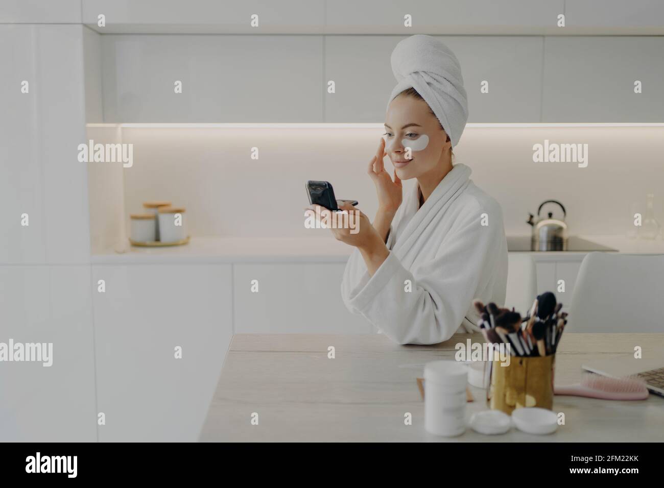 Femme heureuse avec peignoir blanc et serviette sur la tête taches cosmétiques sous les yeux Banque D'Images