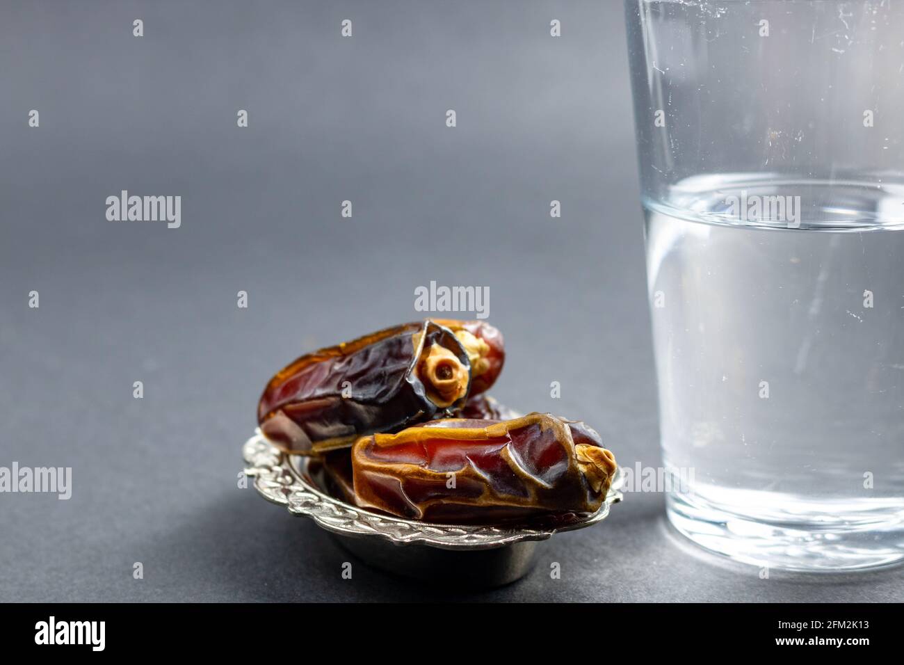 Mise au point sélective des dates et d'un verre d'eau sur fond gris. Photo de haute qualité. Aliments et en-cas du ramadan. Fête de l'iftar. Jeûne en ramadan. Banque D'Images