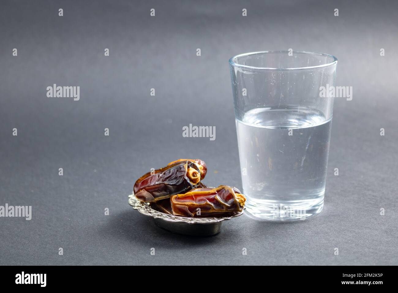 dates sur le bol et un verre d'eau sur fond gris. Photo de haute qualité. Aliments et en-cas du ramadan. Fête de l'iftar. Jeûne en ramadan. Banque D'Images