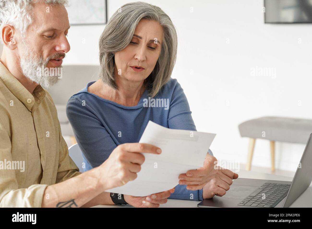 Un couple plus âgé vérifie des documents bancaires ou des factures à l'aide d'un ordinateur portable à la maison. Banque D'Images