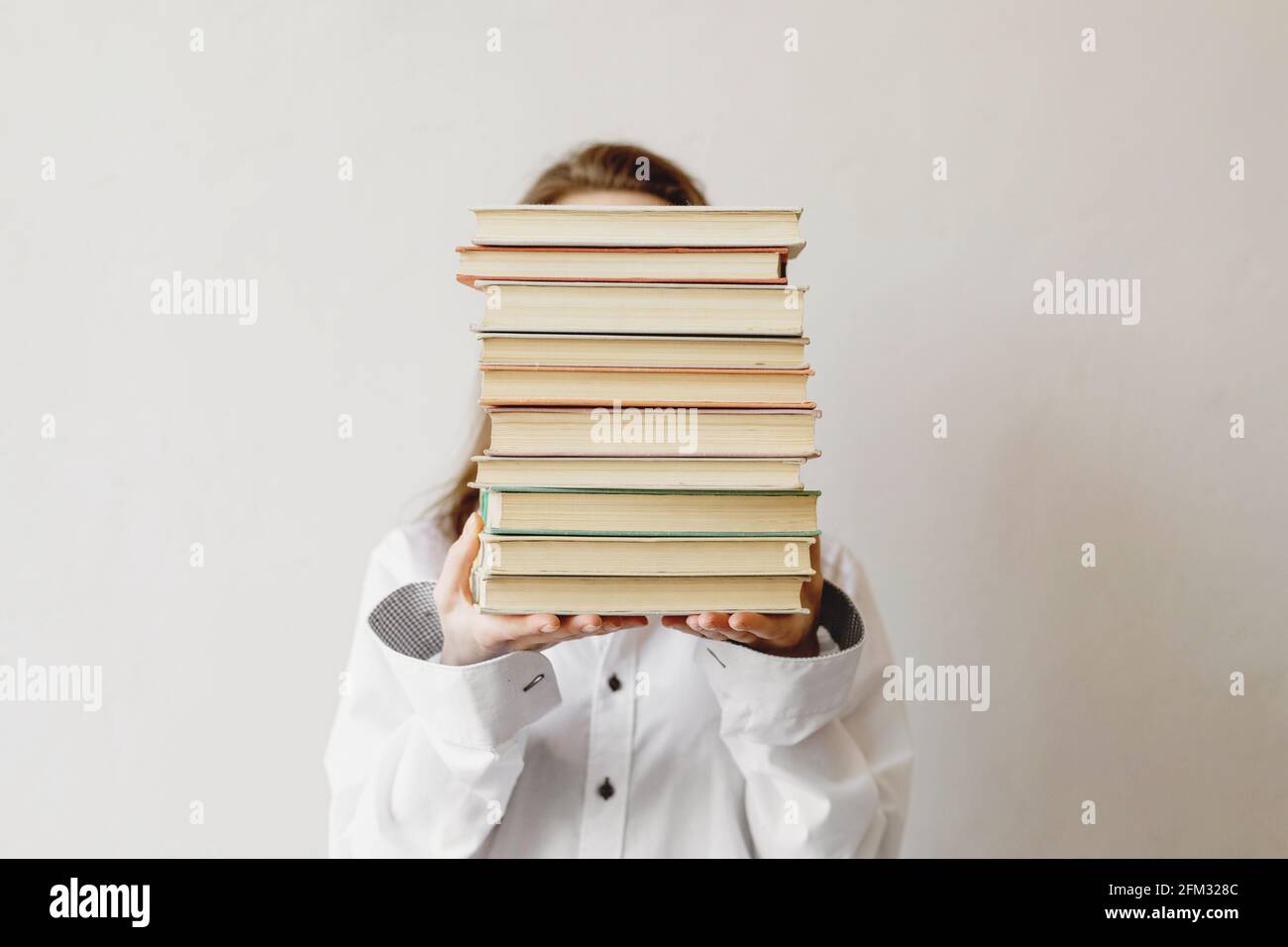 Une jeune étudiante se cache derrière une pile de livres. Banque D'Images