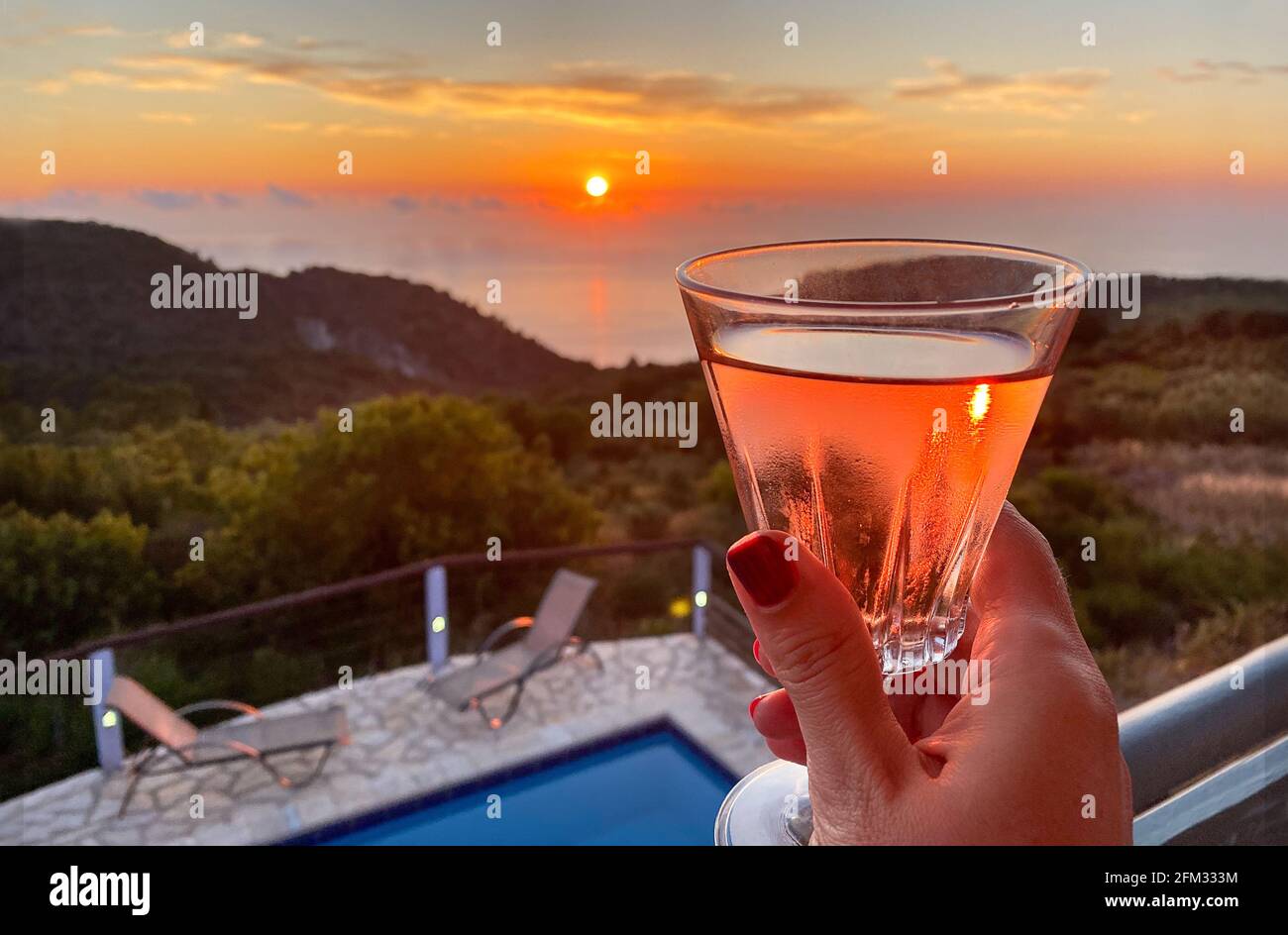 Femme sur un balcon en dégustant un verre de vin au coucher du soleil, Lefkada, Grèce Banque D'Images