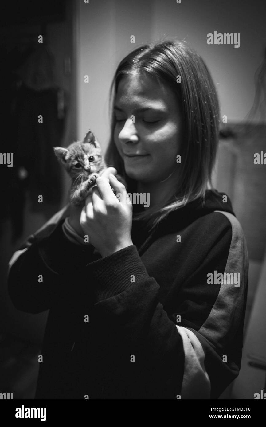 Prise de vue verticale en niveaux de gris d'une jeune femme caucasienne posant avec son joli petit chaton Banque D'Images