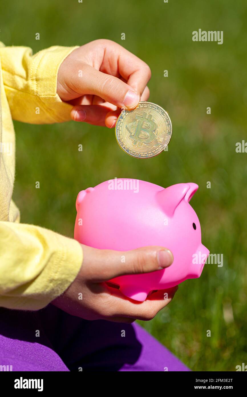 une fille caucasienne met une pièce symbolique en bitcoin dans sa banque de pigeons. Image de concept pour les enfants qui économisent la crypto-monnaie pour l'avenir. Elle tient la piggy Banque D'Images
