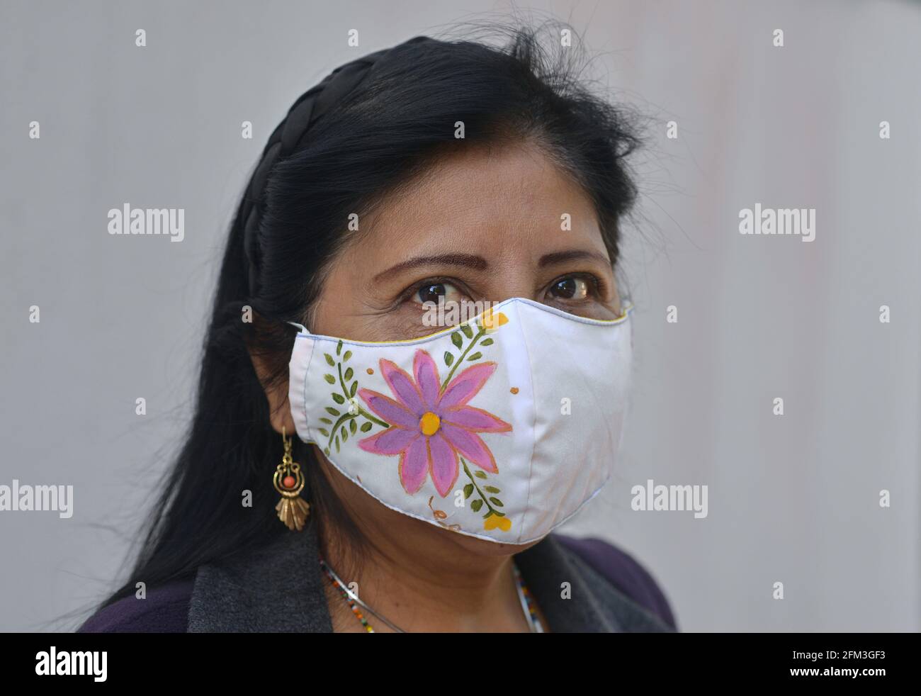 Mature jolie femme mexicaine avec de beaux yeux bruns porte un masque de tissu peint à la main pendant la pandémie de coronavirus et regarde le spectateur. Banque D'Images