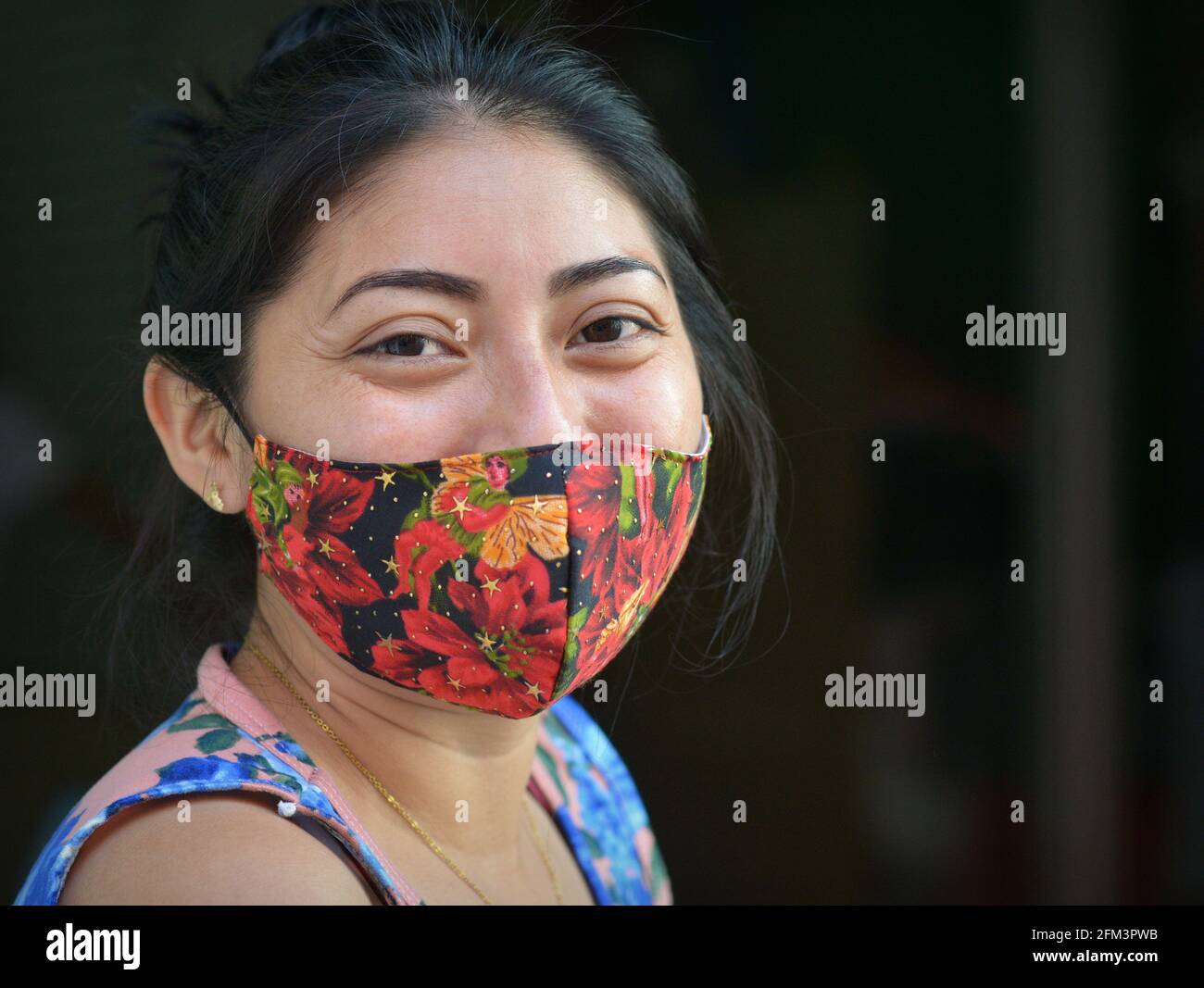 Charmante jeune femme mexicaine positive aux yeux bruns souriants porte un masque facial en tissu non médical coloré pendant la pandémie du coronavirus. Banque D'Images
