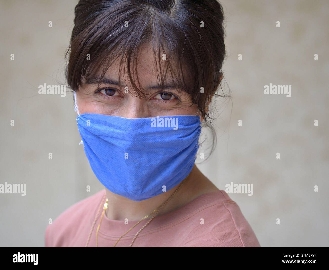 Une jeune femme caucasienne aux yeux bruns souriants porte un masque facial en tissu bleu non médical autofabriqué pendant la pandémie mondiale de coronavirus. Banque D'Images