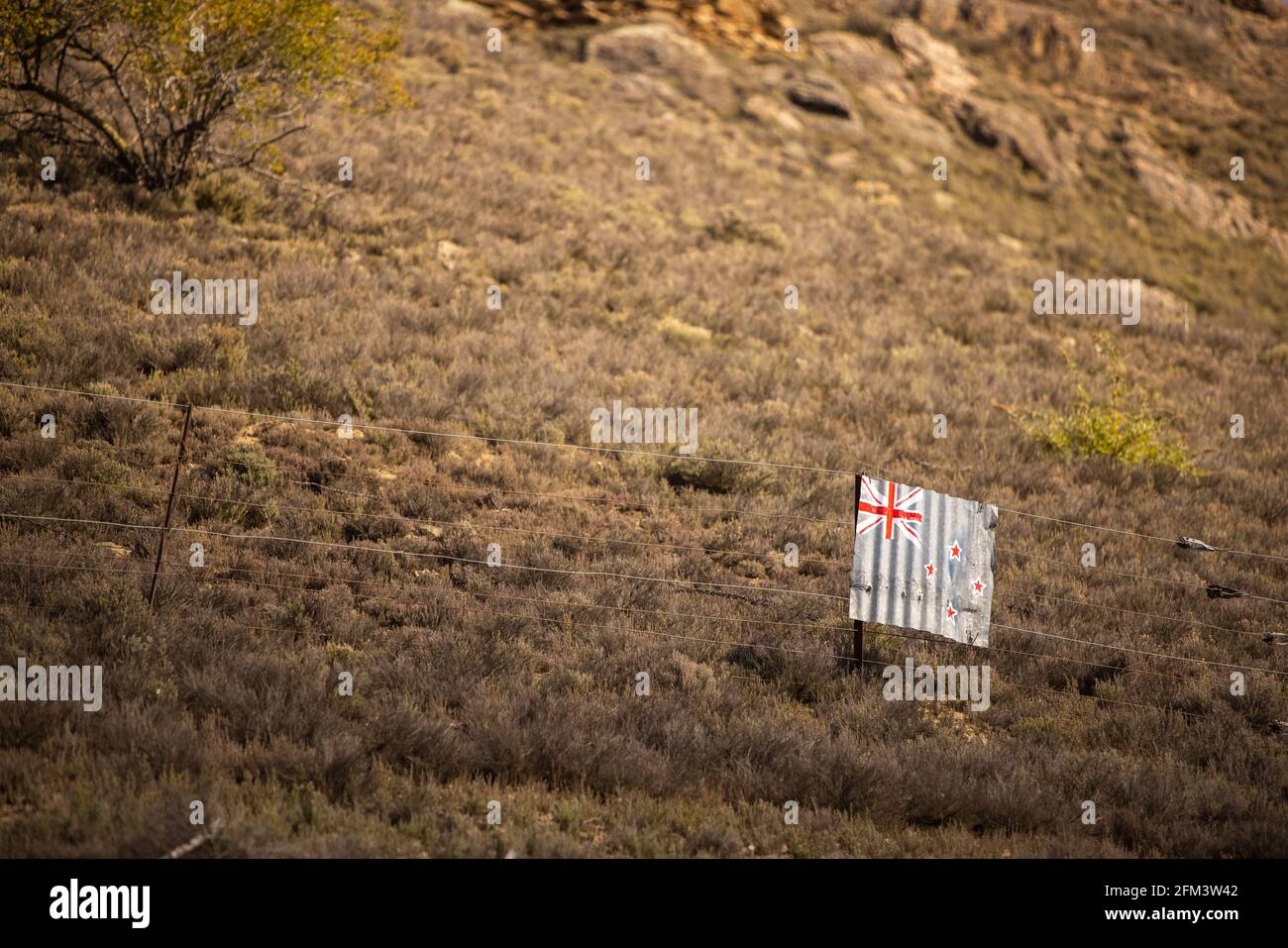Drapeau de la Nouvelle-Zélande peint sur du fer ondulé suspendu sur une clôture en fil de fer dans des terres agricoles accidentées, Central Otago, South Island, Nouvelle-Zélande Banque D'Images