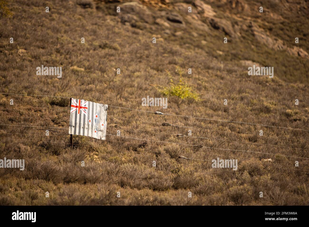 Drapeau de la Nouvelle-Zélande peint sur du fer ondulé en bosselé suspendu sur une clôture en fil de fer dans des terres agricoles accidentées, Central Otago, South Island, Nouvelle-Zélande Banque D'Images