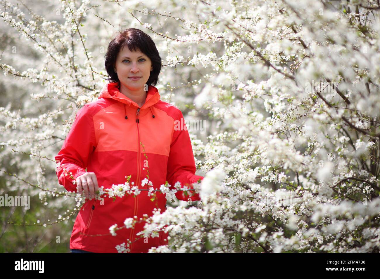 Belle femme mûre posant pour la caméra dans un jardin de printemps fleuri. Banque D'Images