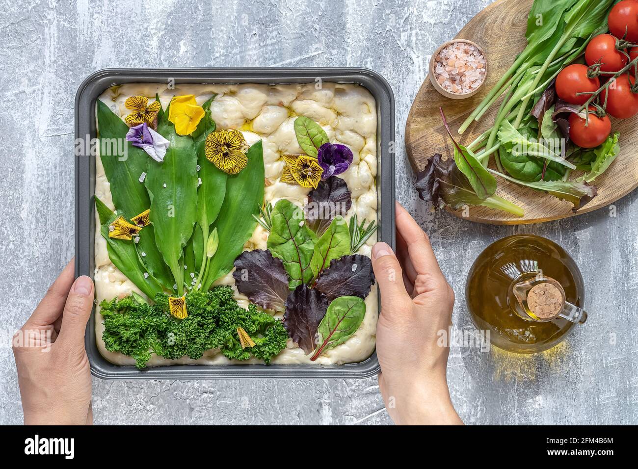 Mains de femmes décorant la focaccia de peinture florale brute, l'art de levain de jardin avec des feuilles d'ail sauvage de saison. Banque D'Images
