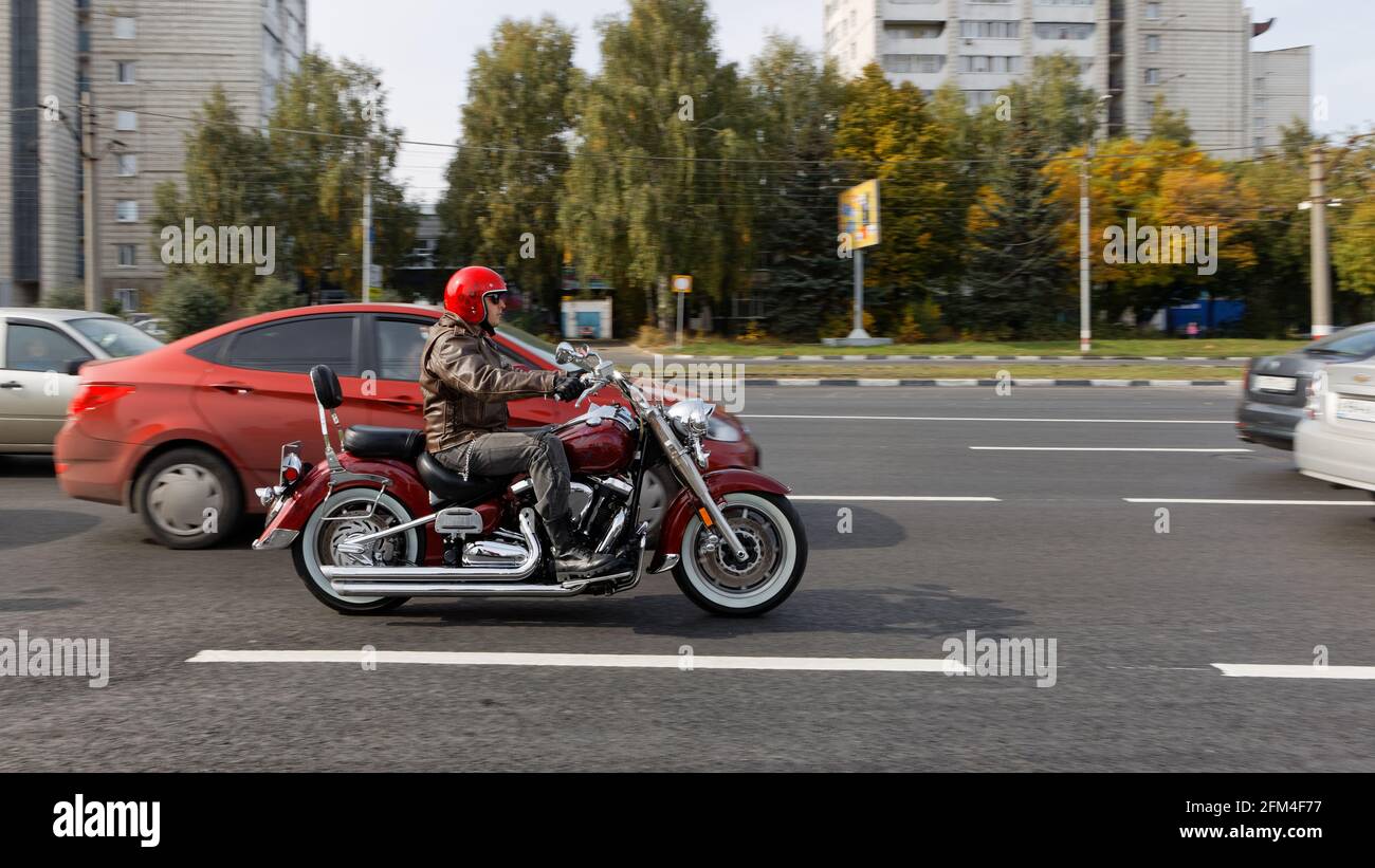 Ulyanovsk, Russie - 26 septembre 2020. Un automobiliste dans un casque rouge fait une moto parmi les voitures le long d'une rue de la ville Banque D'Images Ulyanovsk, Russie - 26 septembre 2020. Un automobiliste dans un casque rouge fait une moto parmi les voitures le long d'une rue de la ville Banque D'Images