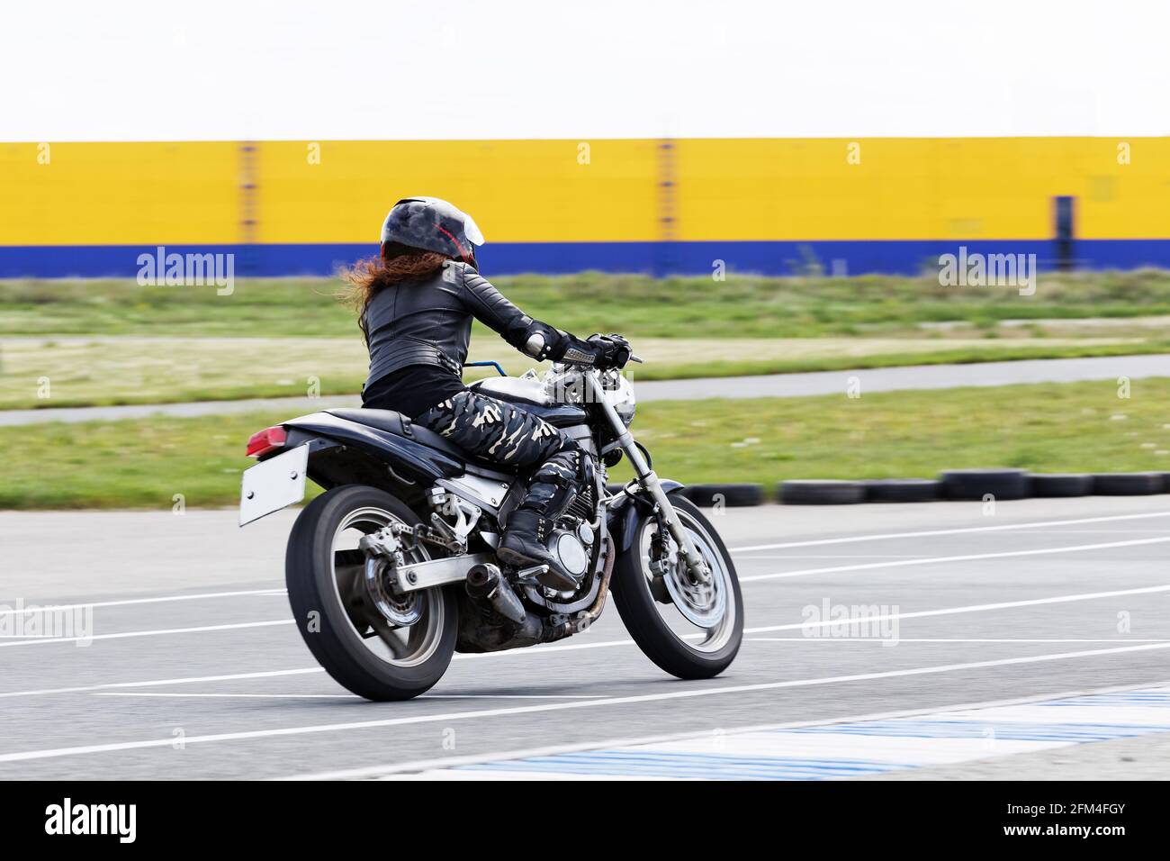 Ulyanovsk, Russie - 10 juin 2017. La jeune fille aux cheveux rouges dans une veste noire et un pantalon de camouflage race sur une moto sur une piste de sport. Flou de mouvement. Banque D'Images