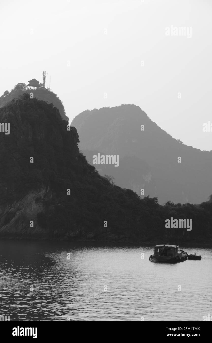 Vue panoramique du coucher de soleil sur les eaux étincelantes, les formations rocheuses, les montagnes bleues et les bateaux flottants sur la baie de Halong au Vietnam Banque D'Images