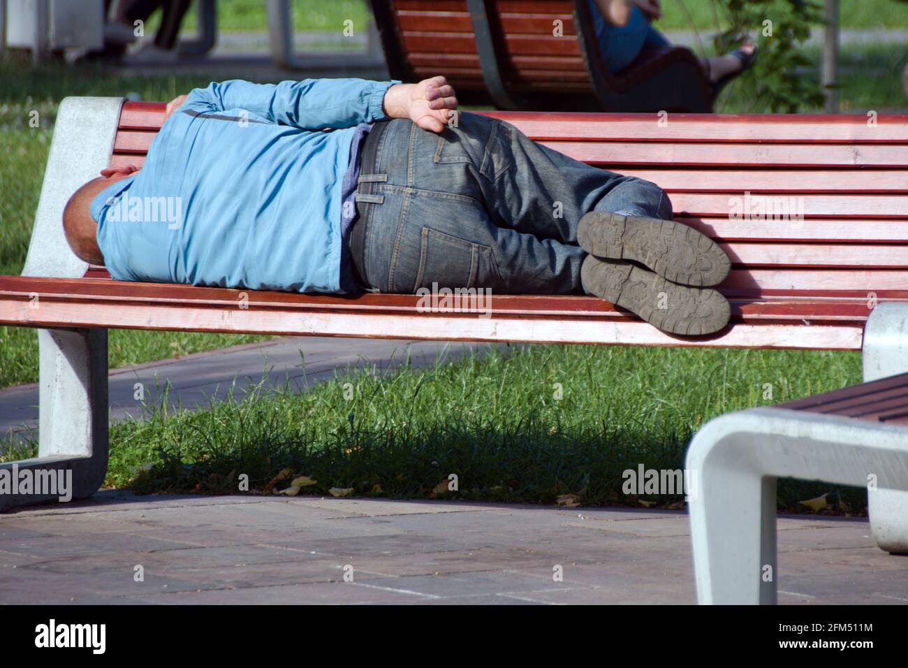 homme sans abri dormant sur le banc du parc par beau temps Banque D'Images