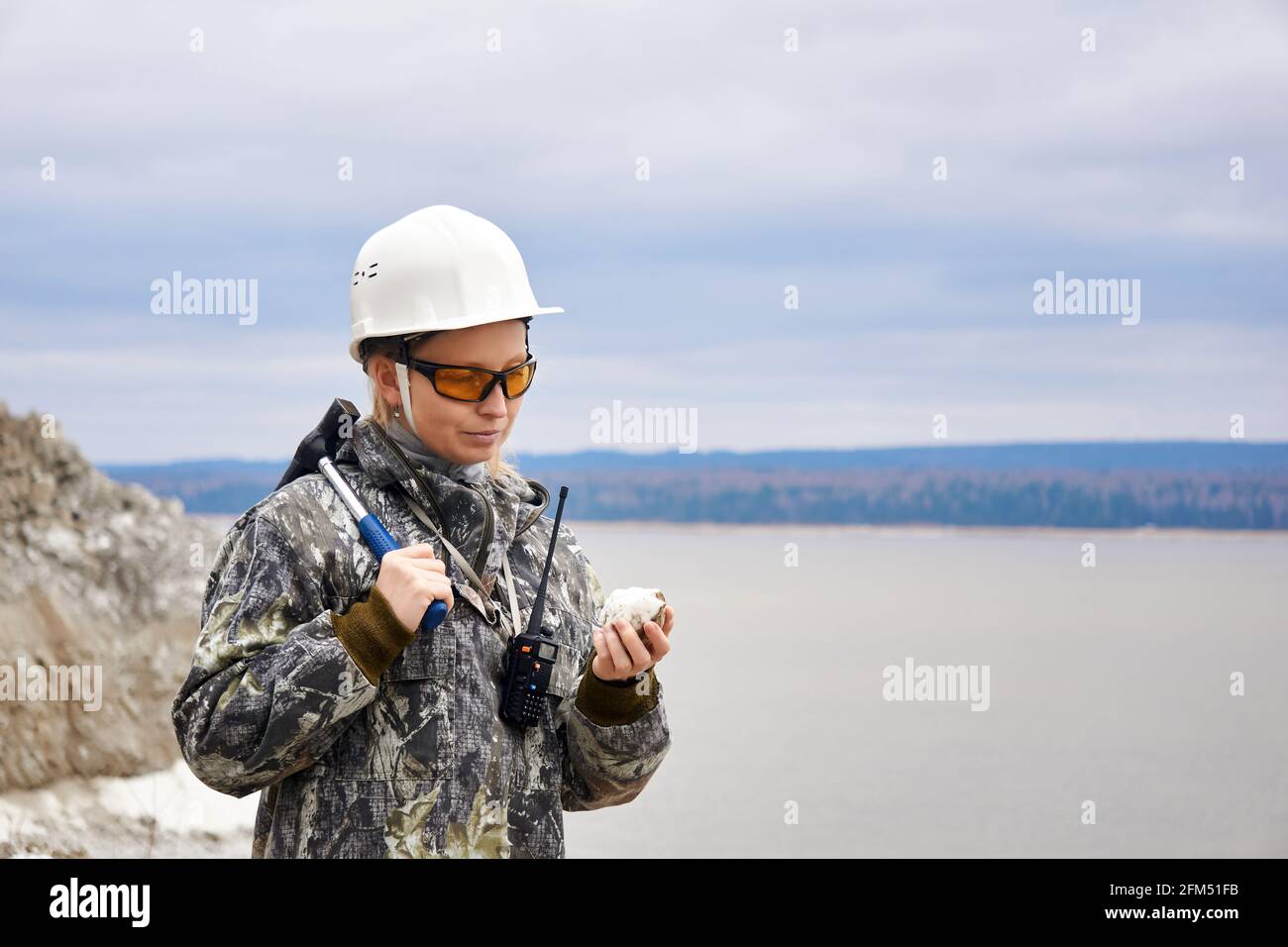 une géologue examine un échantillon de minéraux sur le fond de la fosse ouverte au bord d'une montagne Banque D'Images