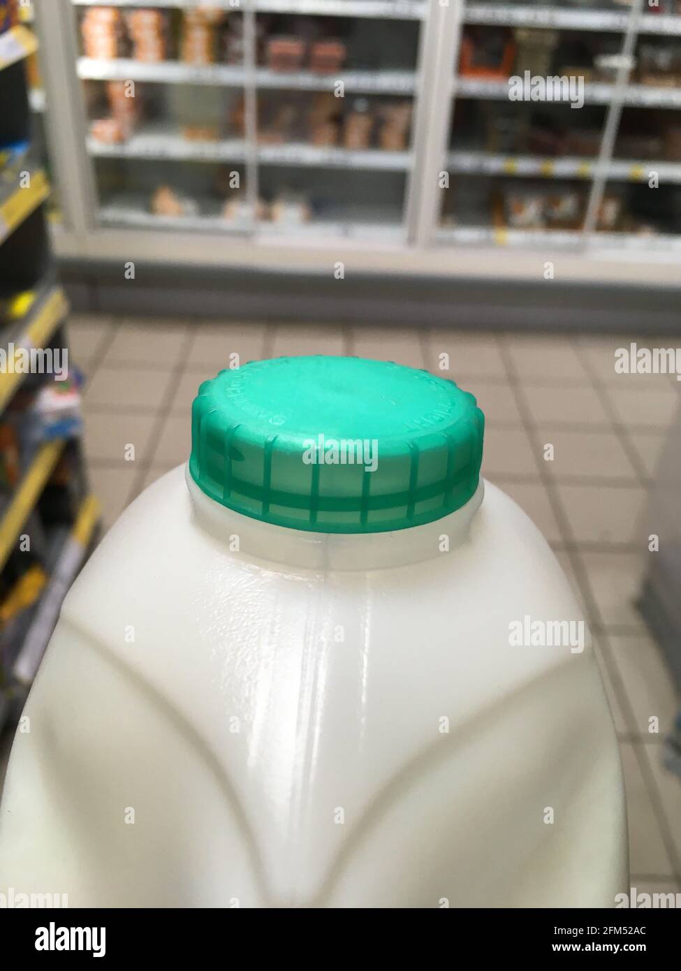 Un carton de lait pasteurisé demi-écrémé britannique avec un dessus de bouteille vert transporté d'une étagère à la caisse dans un supermarché. Le client achète le lait à la boutique. ROYAUME-UNI. (123) Banque D'Images