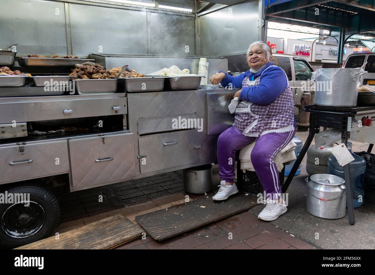 Une femme sud-américaine qui exploite un stand de nourriture chaude prend une pause déjeuner. Sous le métro surélevé de Corona, Queens, New York. Banque D'Images