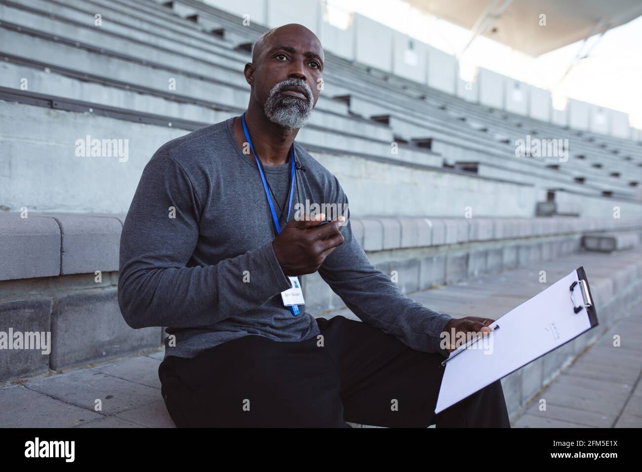 Entraîneur mâle afro-américain avec chronomètre mesurant le temps en position assise sur les sièges dans le stade Banque D'Images