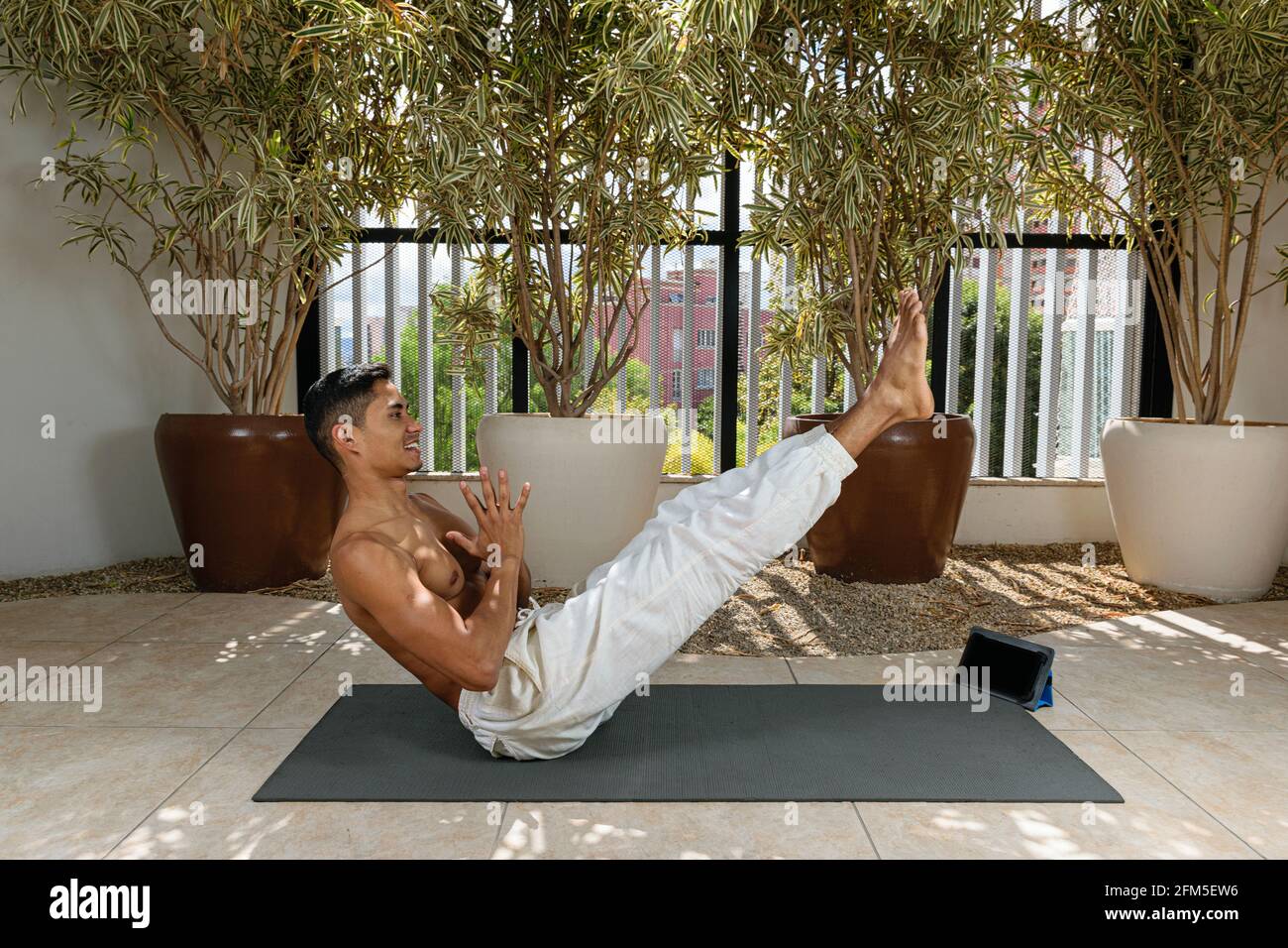 Jeune homme brésilien prenant des cours de yoga en ligne, faisant une position de bateau. Banque D'Images