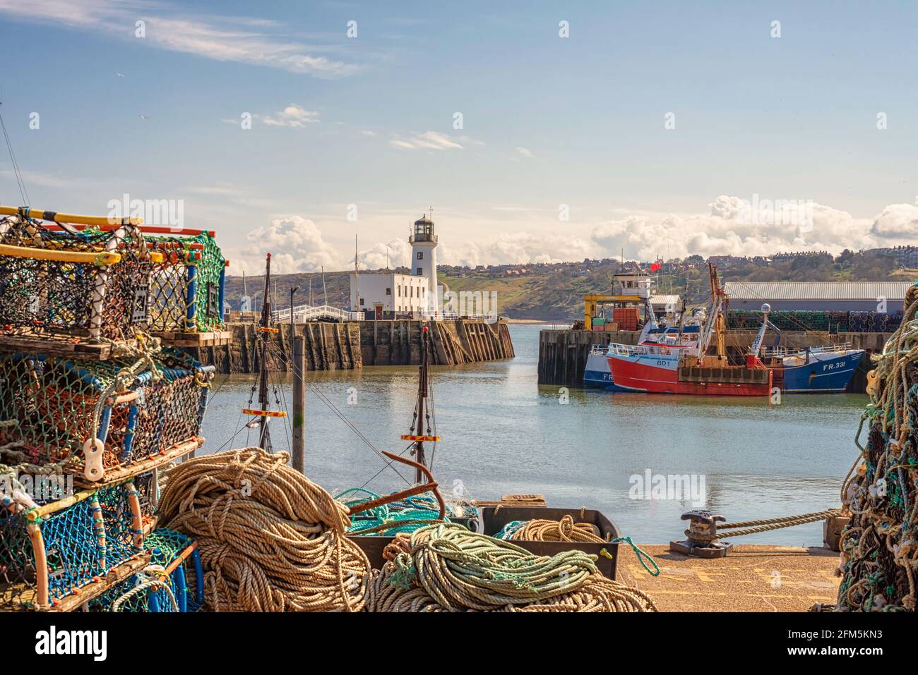 Les bateaux de pêche sont amarrés le long d'un quai et un phare est d'un côté. Une passerelle relie les jetées. Pots et cordes de homard. Banque D'Images