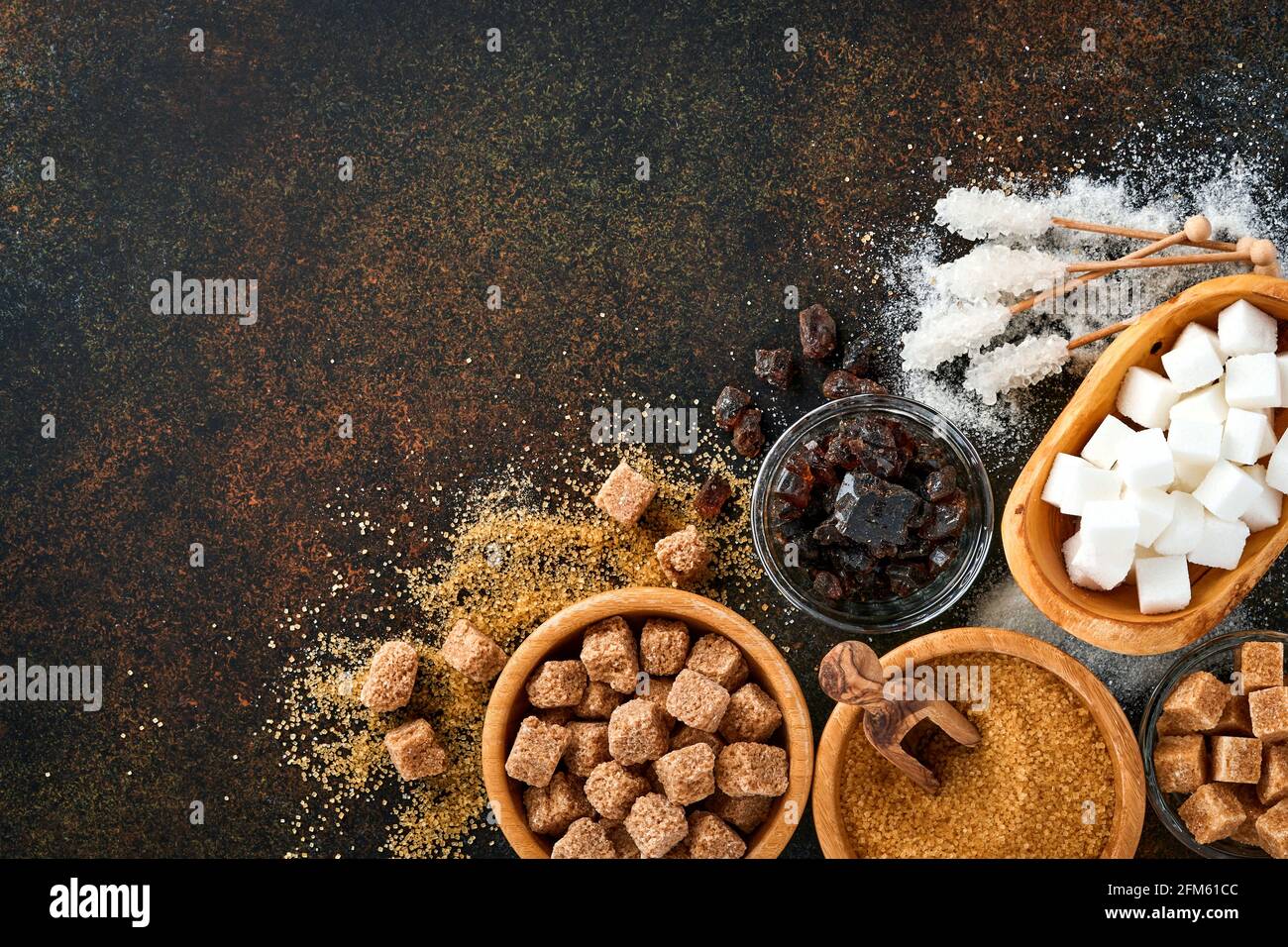 Sucre blanc, cubes de sucre de canne, caramel dans un bol en bambou sur fond de béton de table brun foncé. Différents types de sucre assortis. Vue de dessus ou plan de travail Banque D'Images