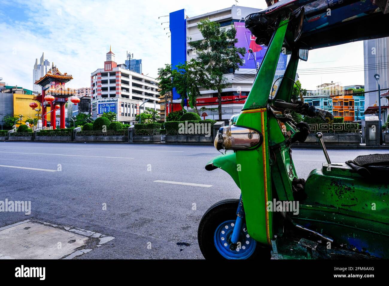 Un tuk-tuk vert se dresse dans la route avec la porte du monument de Chinatown à la distance à Bangkok, en Thaïlande Banque D'Images