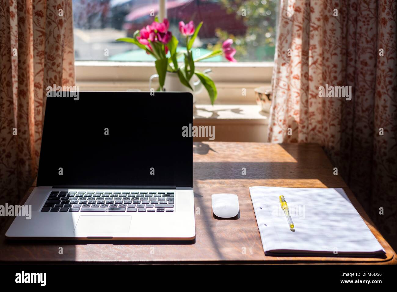 bloc-notes, souris et stylo avec des feuilles sur une table avec des fleurs et une fenêtre en bokeh Banque D'Images