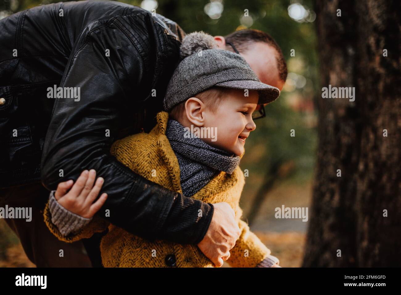 Père et fils ayant hug dans le parc de la ville d'automne. Joyeux enfant  qui marche parmi les feuilles mortes. Mode pour enfants. Garçon portant un  manteau, une casquette et une écharpe