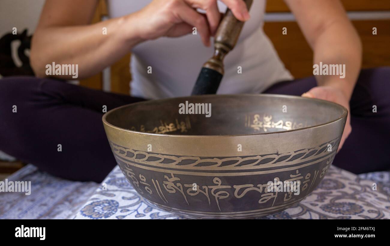 Une femme joue sur un bol de chant décoré avec des signes traditionnels de mantra bouddhiste "louange au joyau dans le Lotus" pour obtenir calme, méditer, écouter. Banque D'Images