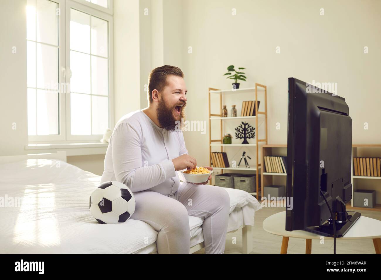 Vue latérale de drôle de ventilateur de football à barbe en train de regarder un match à la télévision à la maison assis sur un canapé. Banque D'Images