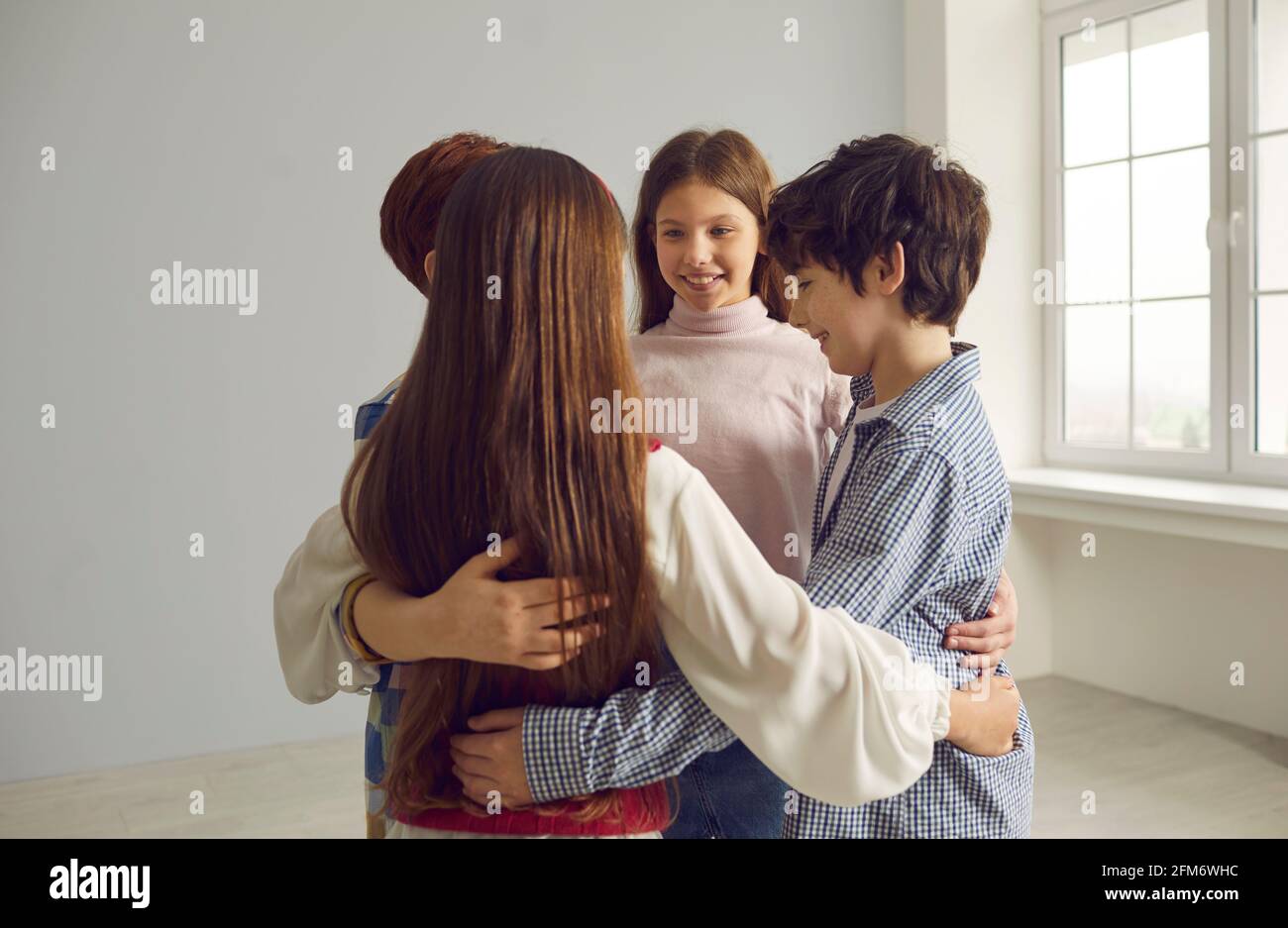 Groupe de quatre enfants heureux positifs de petite école embrassant chacun autre et souriant Banque D'Images