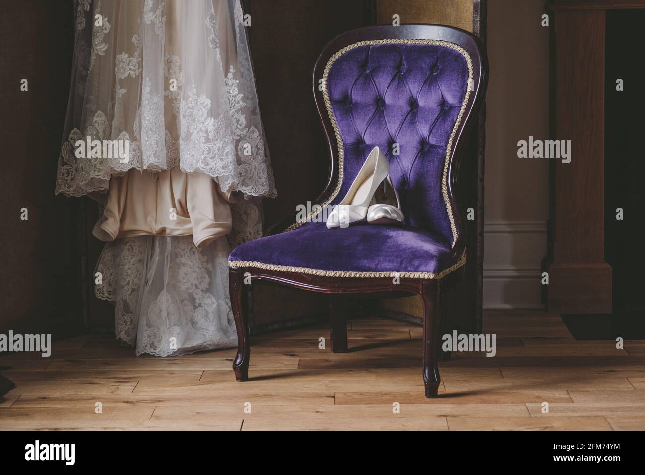 Les chaussures d'une mariée sont assises sur une chaise avec sa robe de mariage à l'arrière-plan Banque D'Images