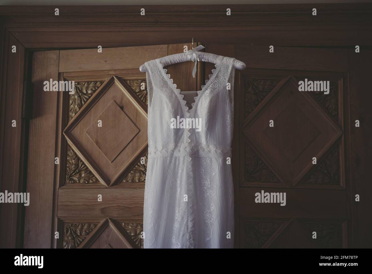 Haut et corsage d'une robe de mariage vintage suspendue contre une porte en bois Banque D'Images