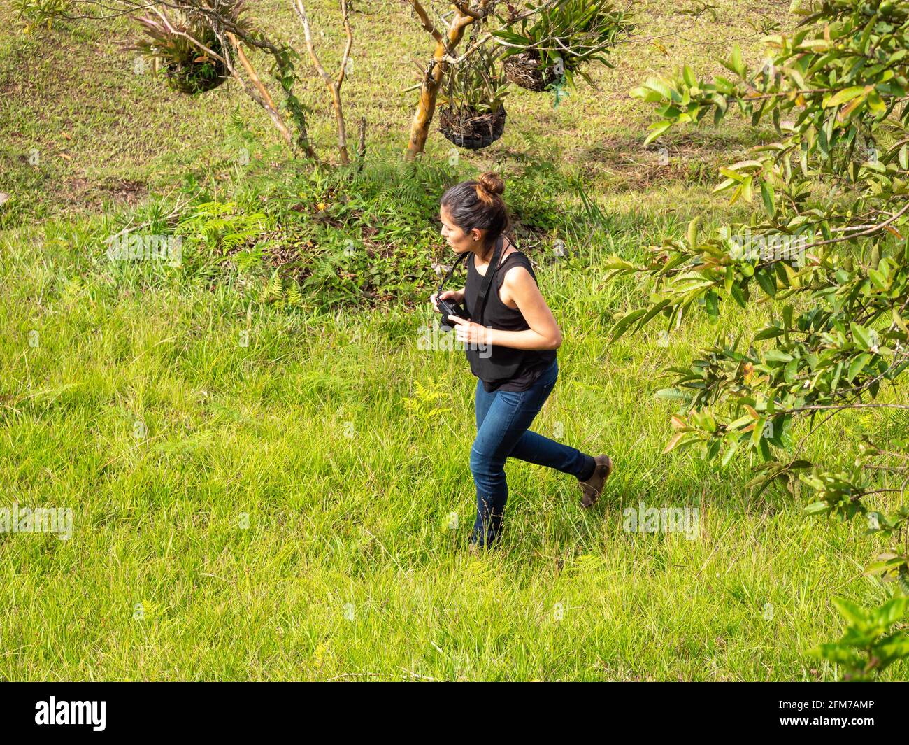 Jeune femme hispanique courte en Jean bleu et chemise noire Prend des photos avec un appareil photo compact sans miroir Banque D'Images