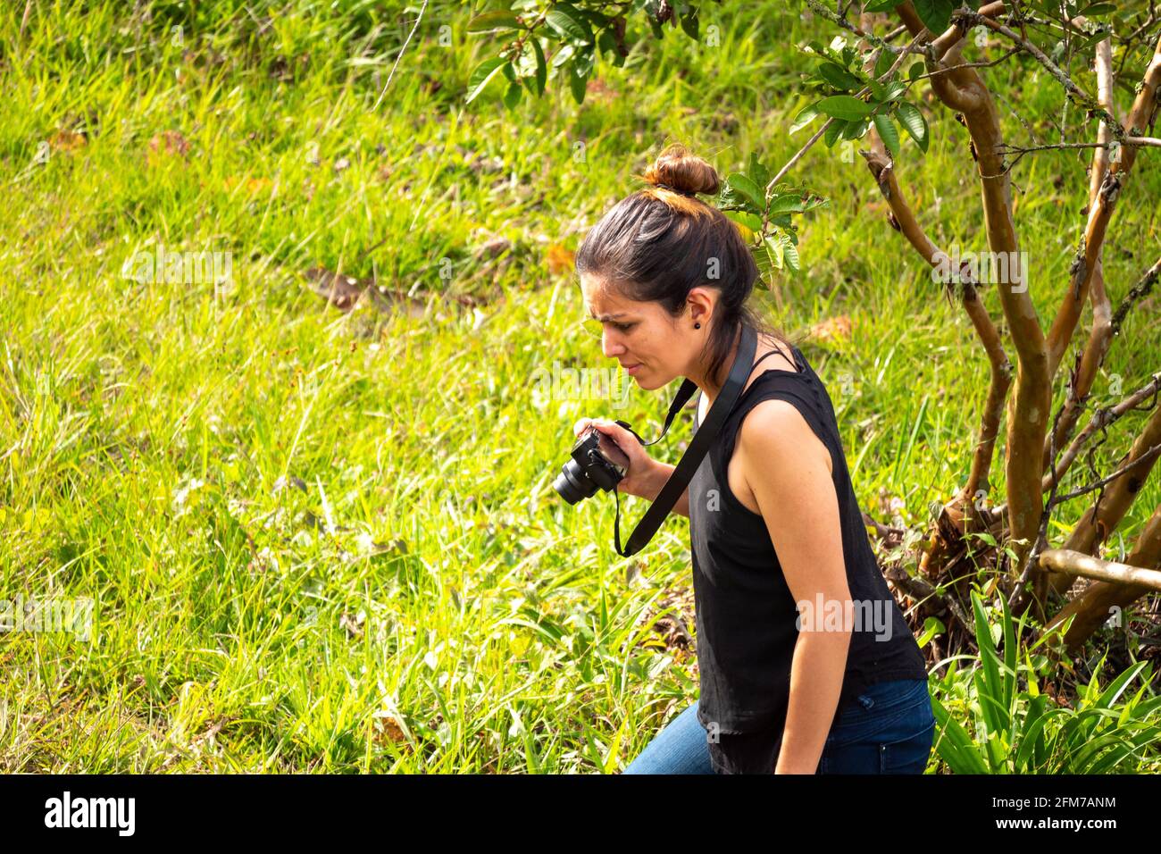 Jeune femme hispanique courte en Jean bleu et chemise noire Prend des photos avec un appareil photo compact sans miroir Banque D'Images