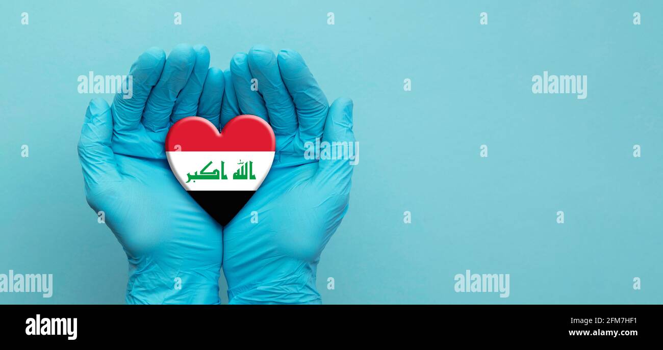 Les mains des médecins portant des gants chirurgicaux tenant le cœur du drapeau irakien Banque D'Images