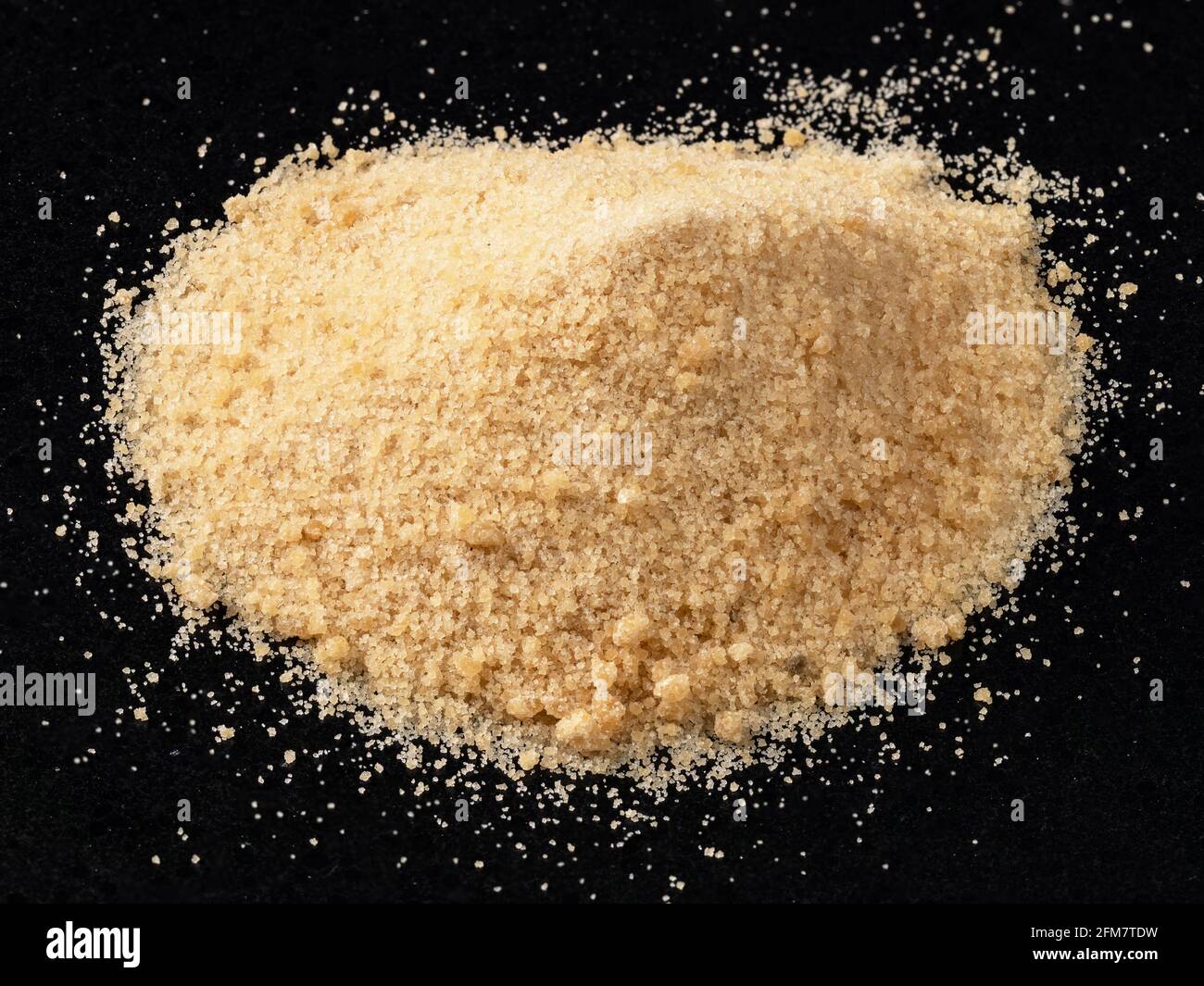 Une poignée de sucre de noix de coco granulé sur une assiette noire Banque D'Images