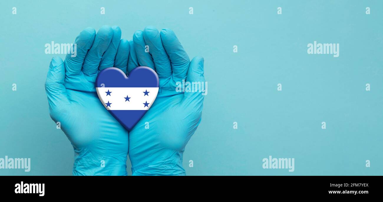 Médecins mains portant des gants chirurgicaux tenant le coeur du drapeau hondurien Banque D'Images