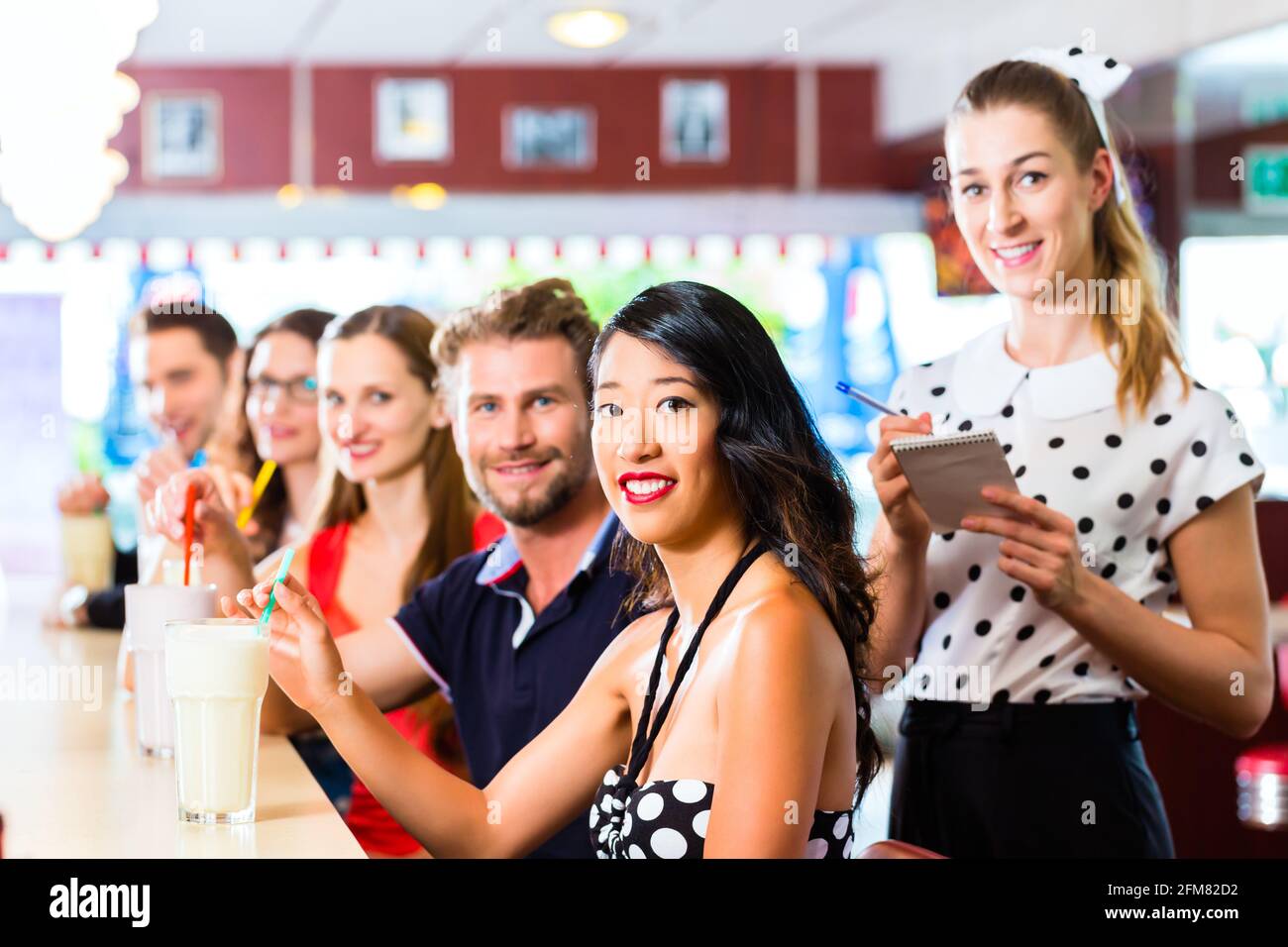 Des amis ou des couples eating fast food et de boire des milk-shakes sur bar en restauration rapide américaine diner, la serveuse est prise des commandes Banque D'Images