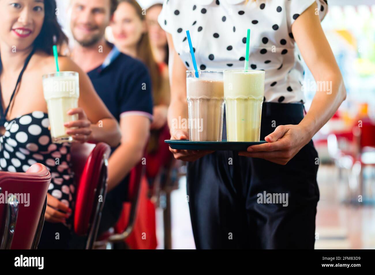 Des amis ou des couples eating fast food et de boire des milk-shakes sur bar en restauration rapide américaine diner, la serveuse est prise des commandes Banque D'Images