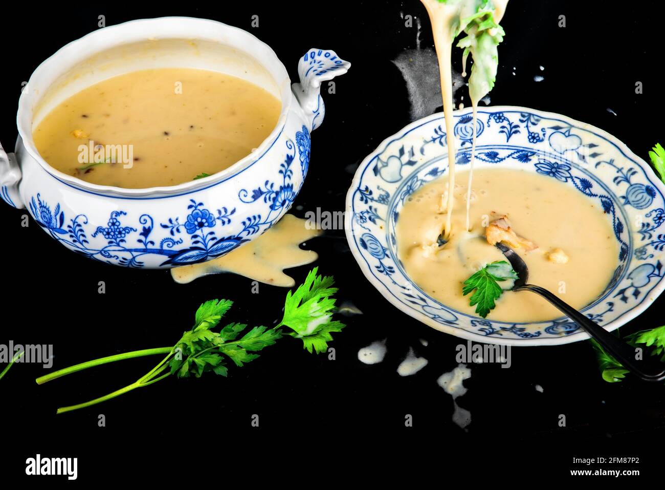 Verser la soupe crémeuse dense de chou-fleur dans un bol de fête avec une louche, une assiette, une feuille de persil, le tout sur fond noir renversé et coloré. Banque D'Images Verser la soupe crémeuse dense de chou-fleur dans un bol de fête avec une louche, une assiette, une feuille de persil, le tout sur fond noir renversé et coloré. Banque D'Images