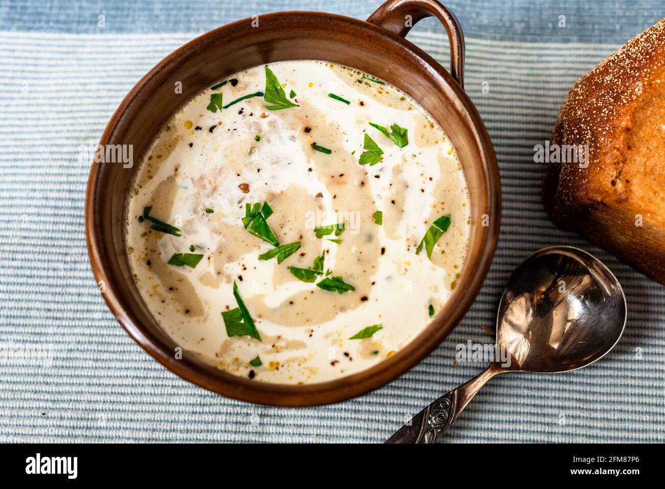 Soupe de légumes crémeuse avec persil dans un bol, cuillère et pain sur un napperon bleu, gros plan. Soupe végétarienne saine. Banque D'Images