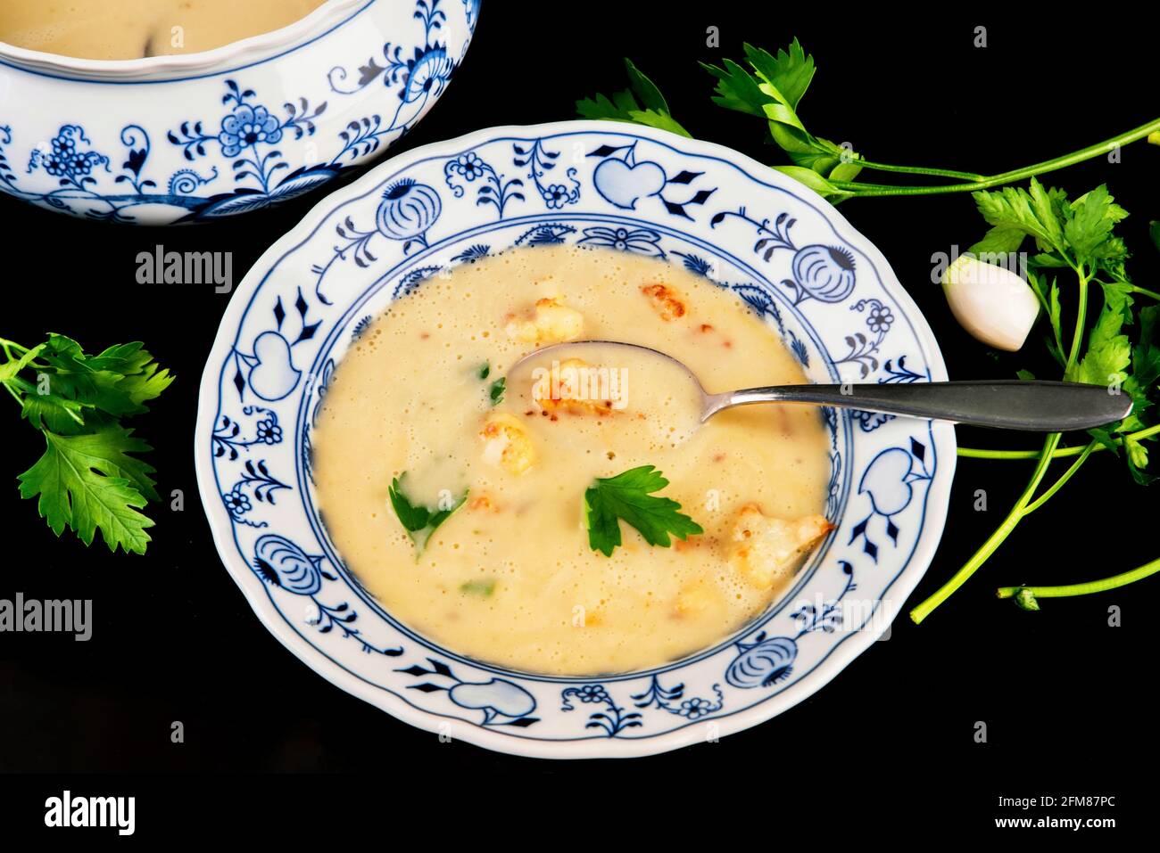 Soupe dense de chou-fleur en assiette décorative en porcelaine, bol, feuille et oignon sur fond noir. Banque D'Images Soupe dense de chou-fleur en assiette décorative en porcelaine, bol, feuille et oignon sur fond noir. Banque D'Images