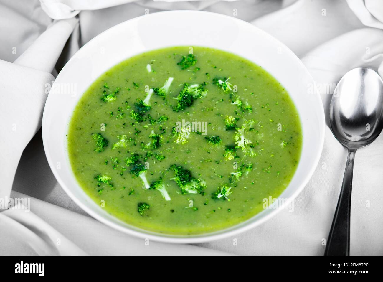 Soupe de brocoli de couleur verte fraîche dans un plat blanc, cuillère sur fond de nappe blanche. Banque D'Images