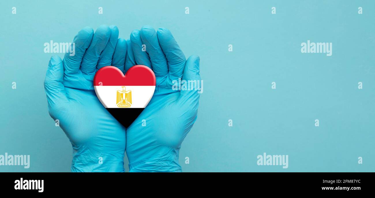 Médecins mains portant des gants chirurgicaux tenant le coeur du drapeau égyptien Banque D'Images