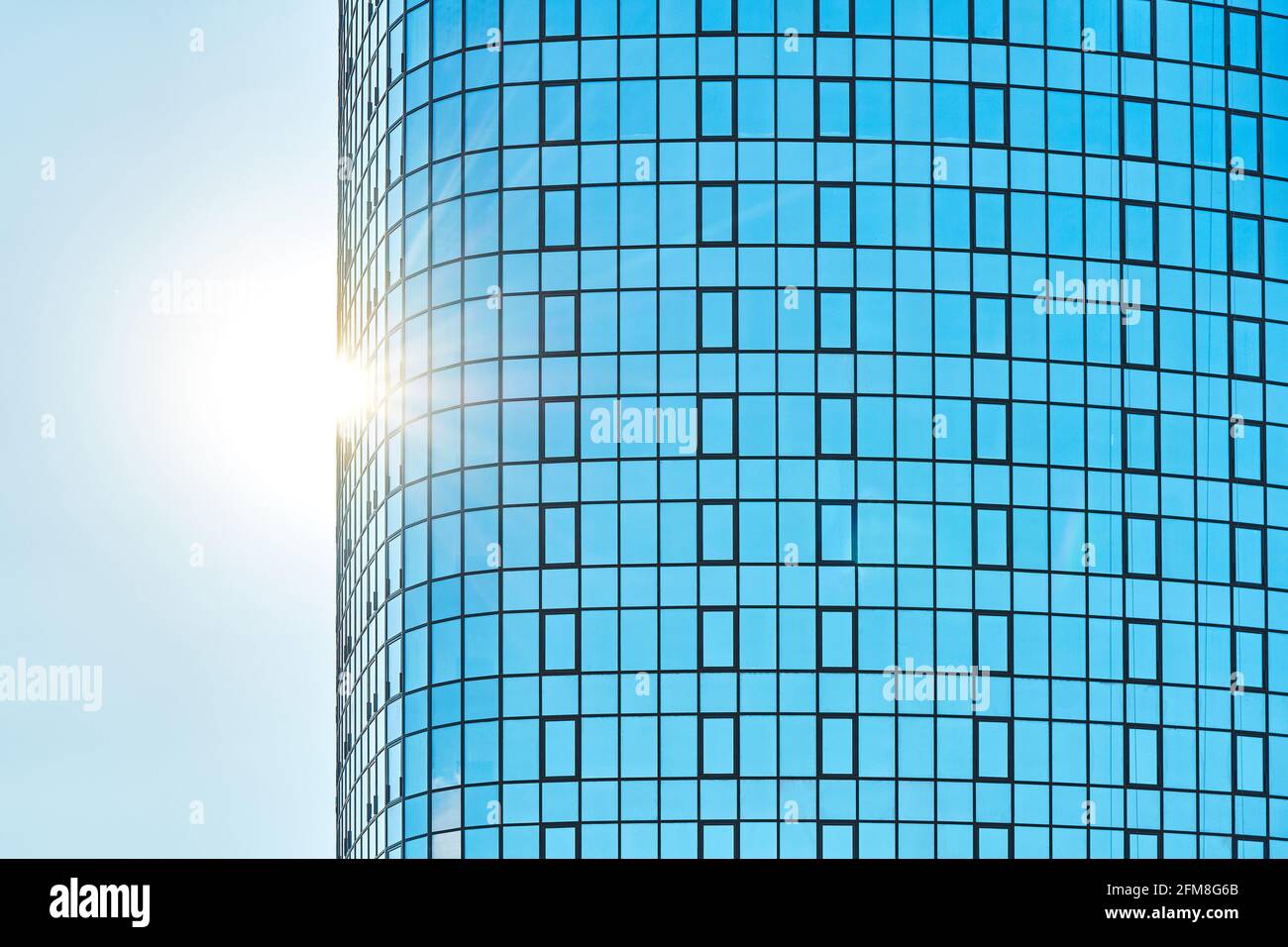Immeuble de bureaux élégant en hauteur avec façade en verre bleu brillant lumière du soleil éclatante contre le ciel bleu clair par temps ensoleillé Banque D'Images
