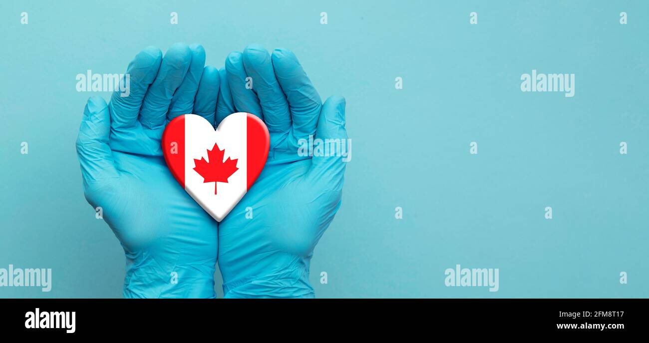 Les médecins mains portant des gants chirurgicaux tenant le cœur du drapeau du Canada Banque D'Images