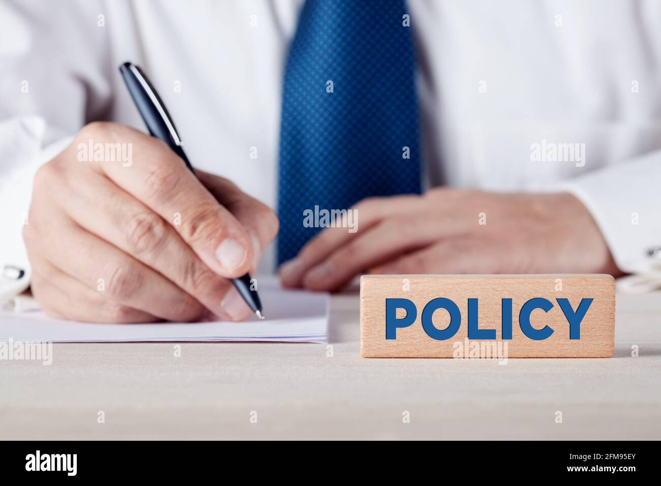Le mot politique écrit sur un bloc de bois avec un homme d'affaires écrit sur une feuille de papier à l'arrière-plan. Concept de police d'assurance. Banque D'Images