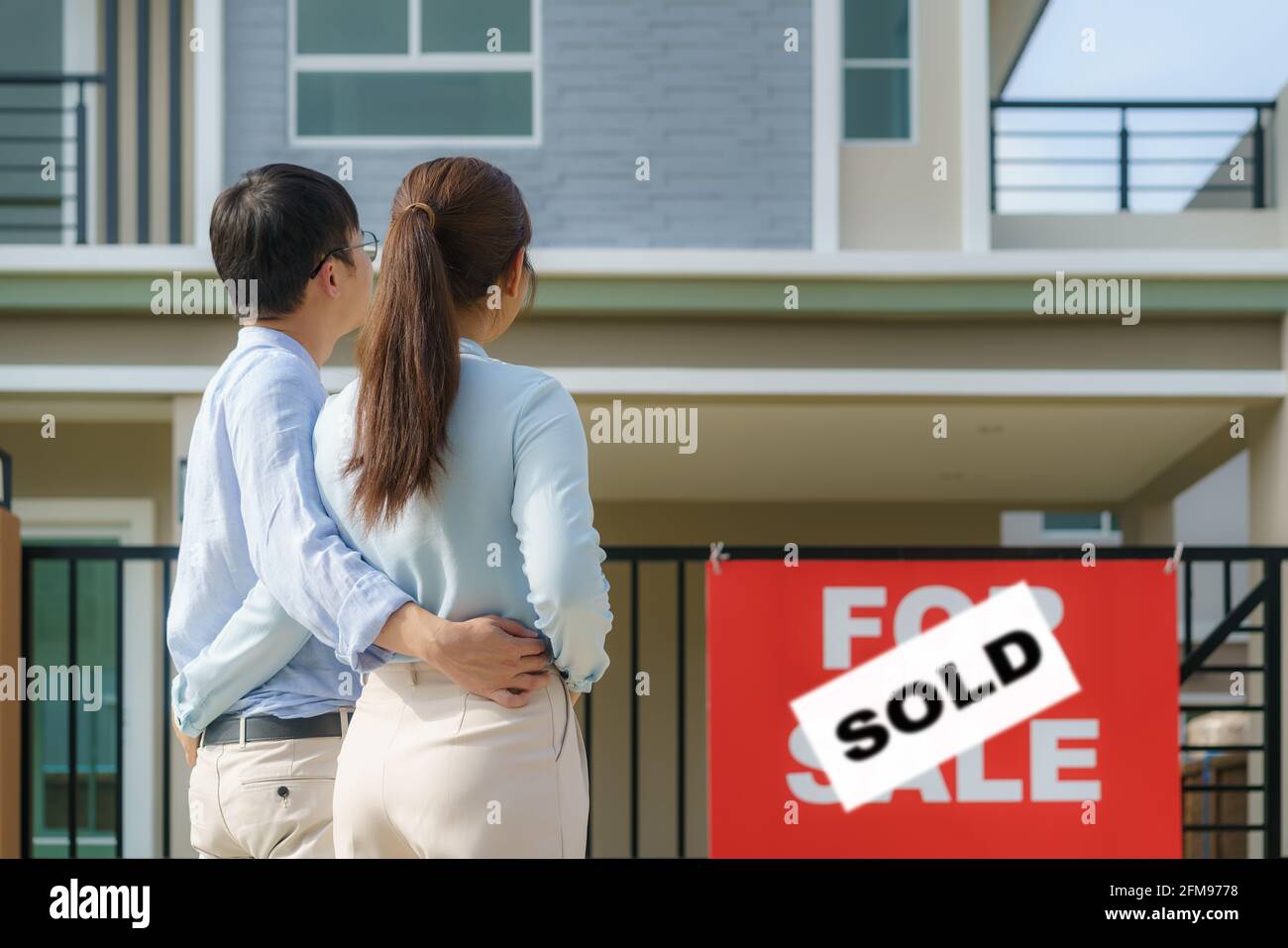 Retour portrait de jeune couple asiatique debout et embrassant ensemble regardant heureux devant leur nouvelle maison pour commencer la nouvelle vie. Famille, âge, maison, réel Banque D'Images